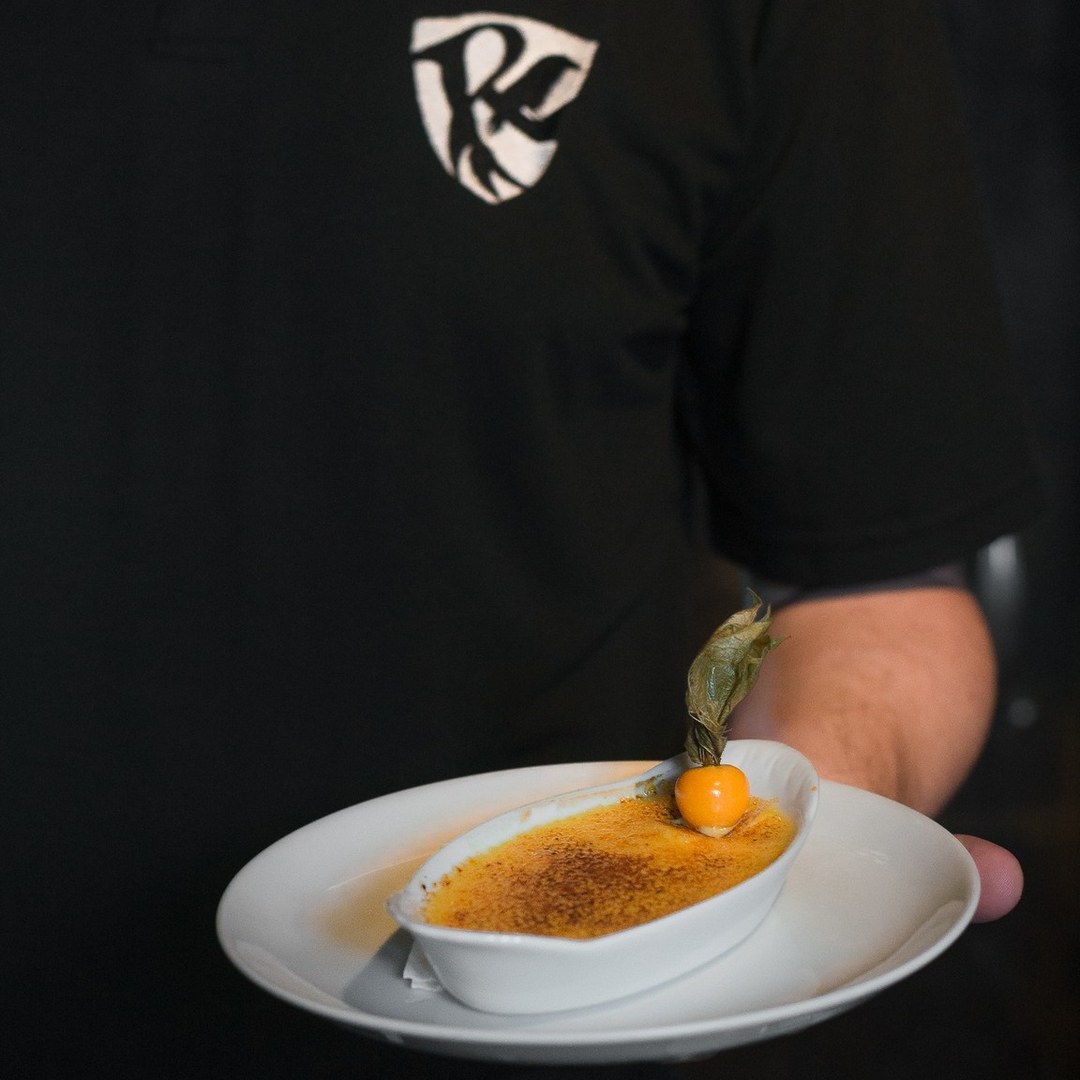 Crème brûlée sendo finalizado à mesa, servido em ramequim branco.