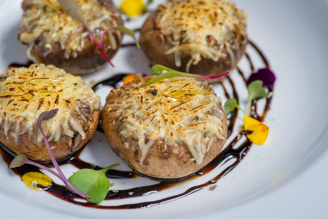 Cogumelos recheados e gratinados com parmesão, com flores comestíveis e redução escura.