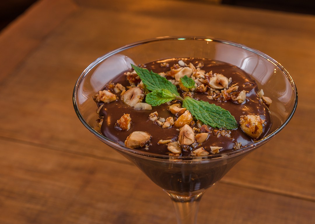 Mousse de chocolate meio amargo servida em taça, com avelãs carameladas e hortelã.