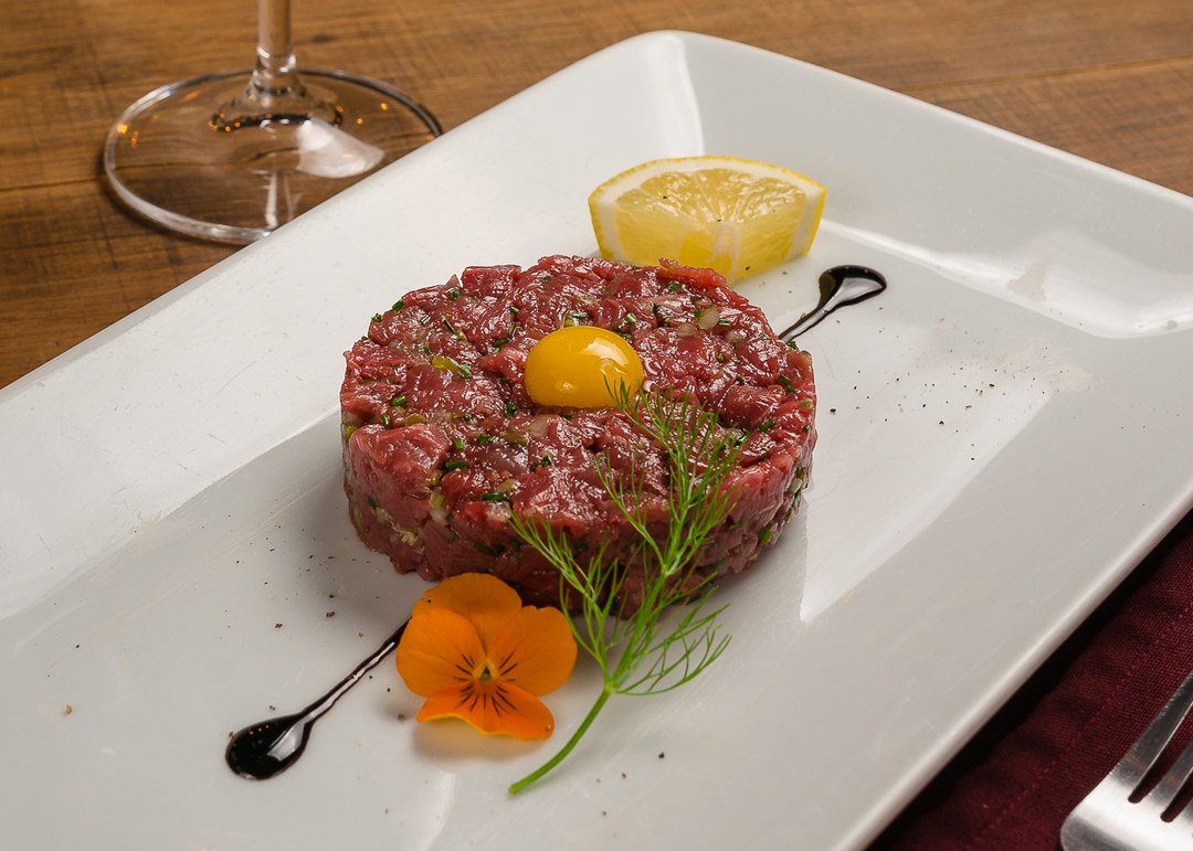 Tartar de filé picado na faca, com gema de ovo de codorna no topo e flor comestível ao lado.